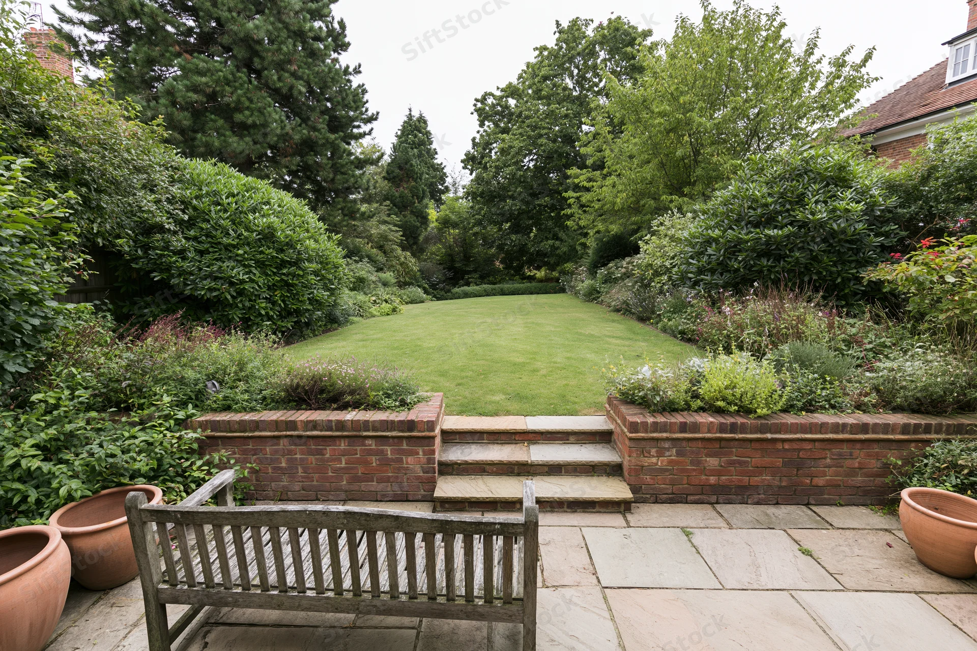 Elevated patio overlooking a manicured lawn bordered by shrubs and trees in a suburban garden