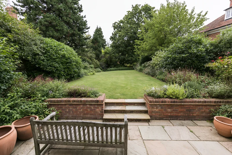 Elevated patio overlooking a manicured lawn bordered by shrubs and trees in a suburban garden
