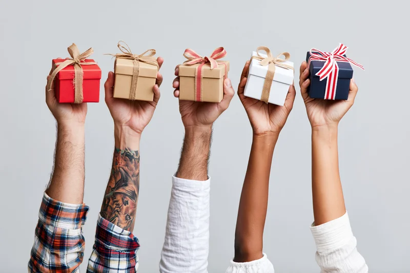 Five diverse hands holding wrapped gift boxes raised upward against a plain background