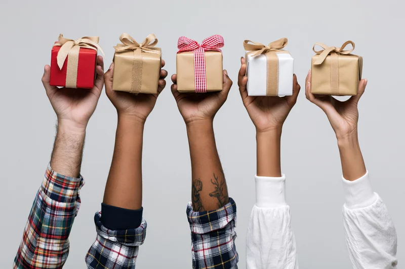 Five diverse hands holding wrapped gifts upward against a plain background