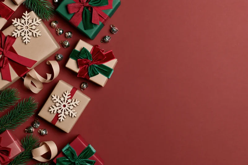 Christmas gift boxes wrapped in kraft paper with ribbons and snowflake ornaments arranged on red surface with copyspace