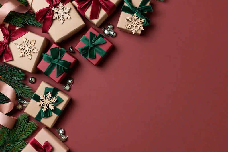 Christmas gift boxes wrapped in kraft paper with ribbons and snowflake ornaments arranged in corner on red background with copyspace