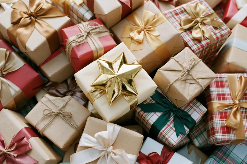 Pile of wrapped christmas gifts with bows and ribbons in various papers and colors filling the frame