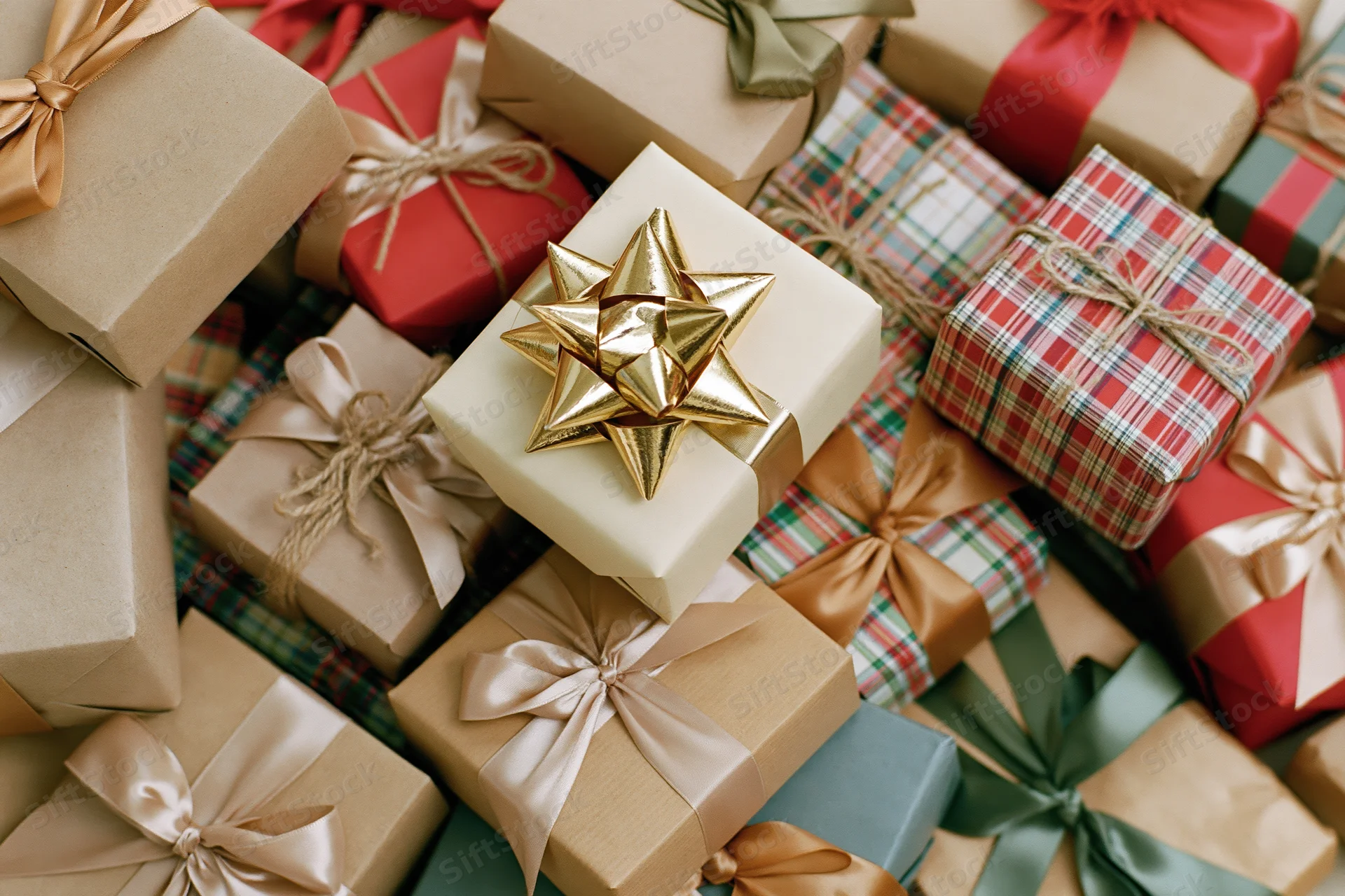Pile of wrapped christmas gifts in various papers and ribbons filling the frame