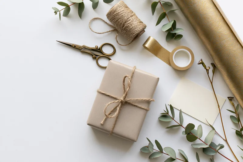 Gift wrapped in kraft paper with twine bow surrounded by wrapping supplies on white surface
