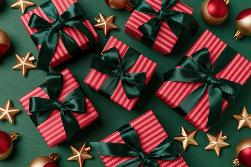 Red striped gift boxes with dark green satin bows arranged on green surface with gold stars and baubles