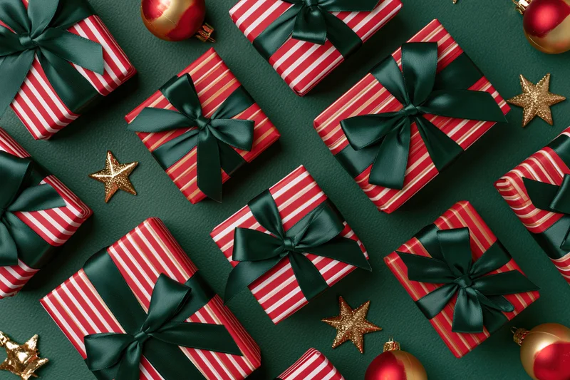 Red and white striped gift boxes with dark green satin bows and gold stars on a dark green surface