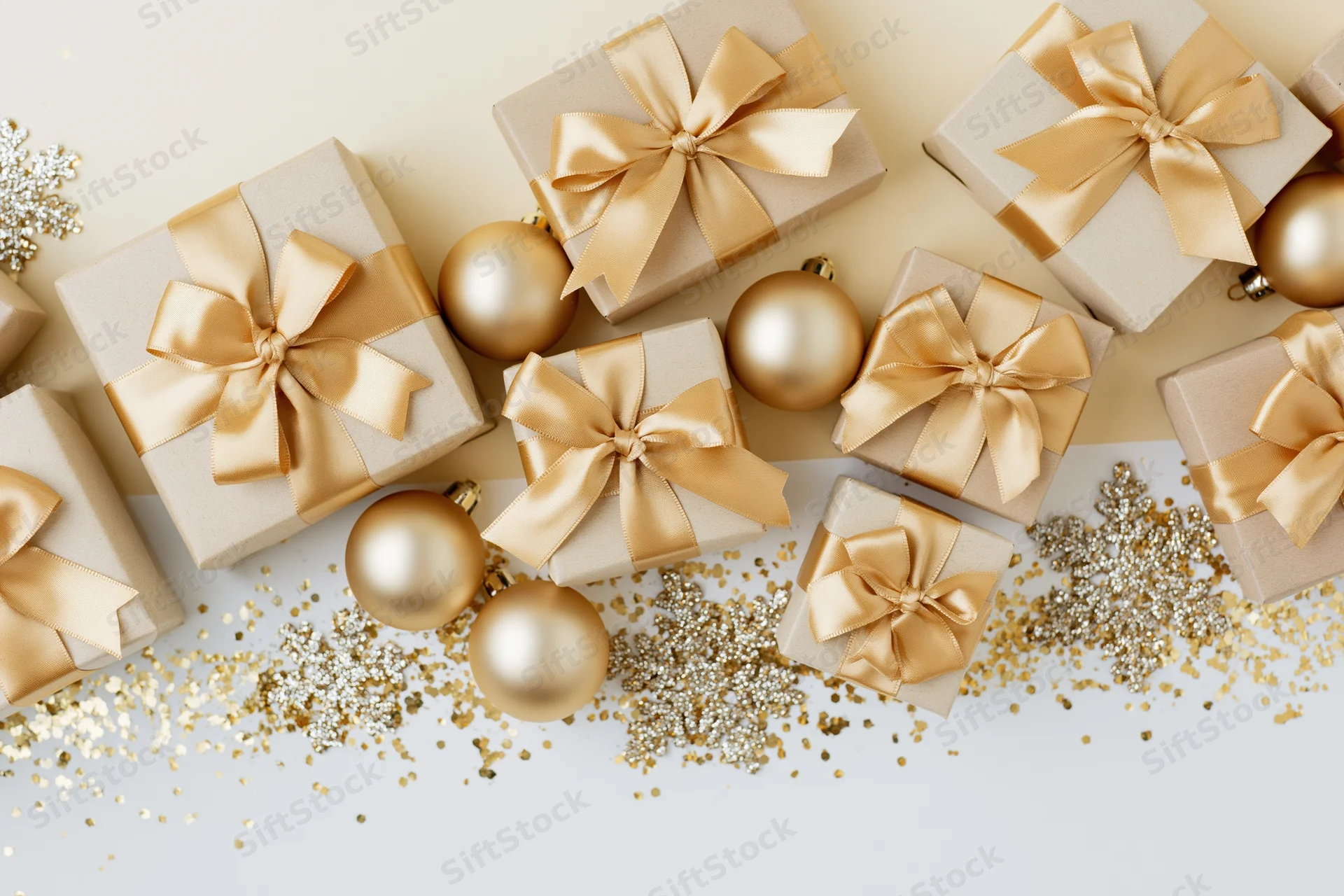 Gift boxes with gold satin ribbon bows and ornaments arranged on a white surface with glitter confetti