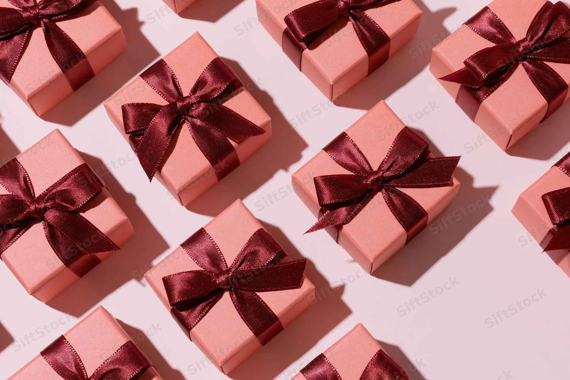 Coral-pink gift boxes with dark red satin bows arranged in a flat lay overhead pattern on a light pink surface