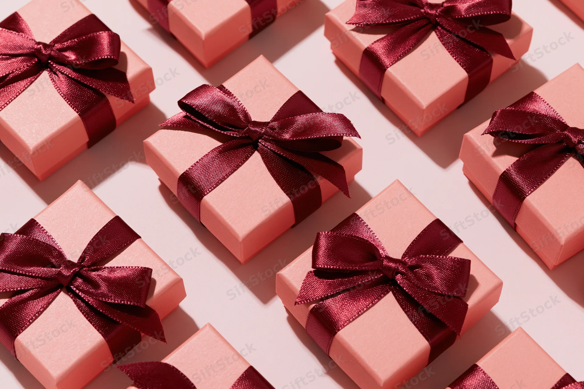 Multiple coral-pink gift boxes with burgundy satin bows arranged in flat lay overhead view on light surface