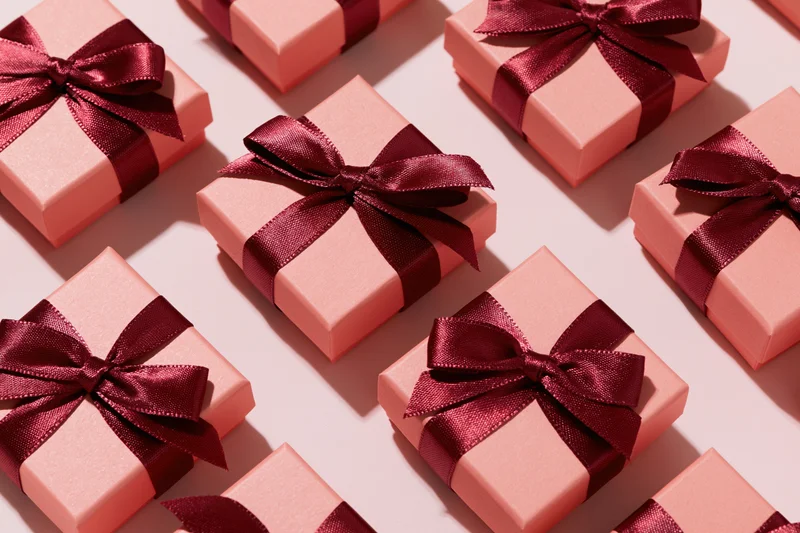 Multiple coral-pink gift boxes with burgundy satin bows arranged in flat lay overhead view on light surface