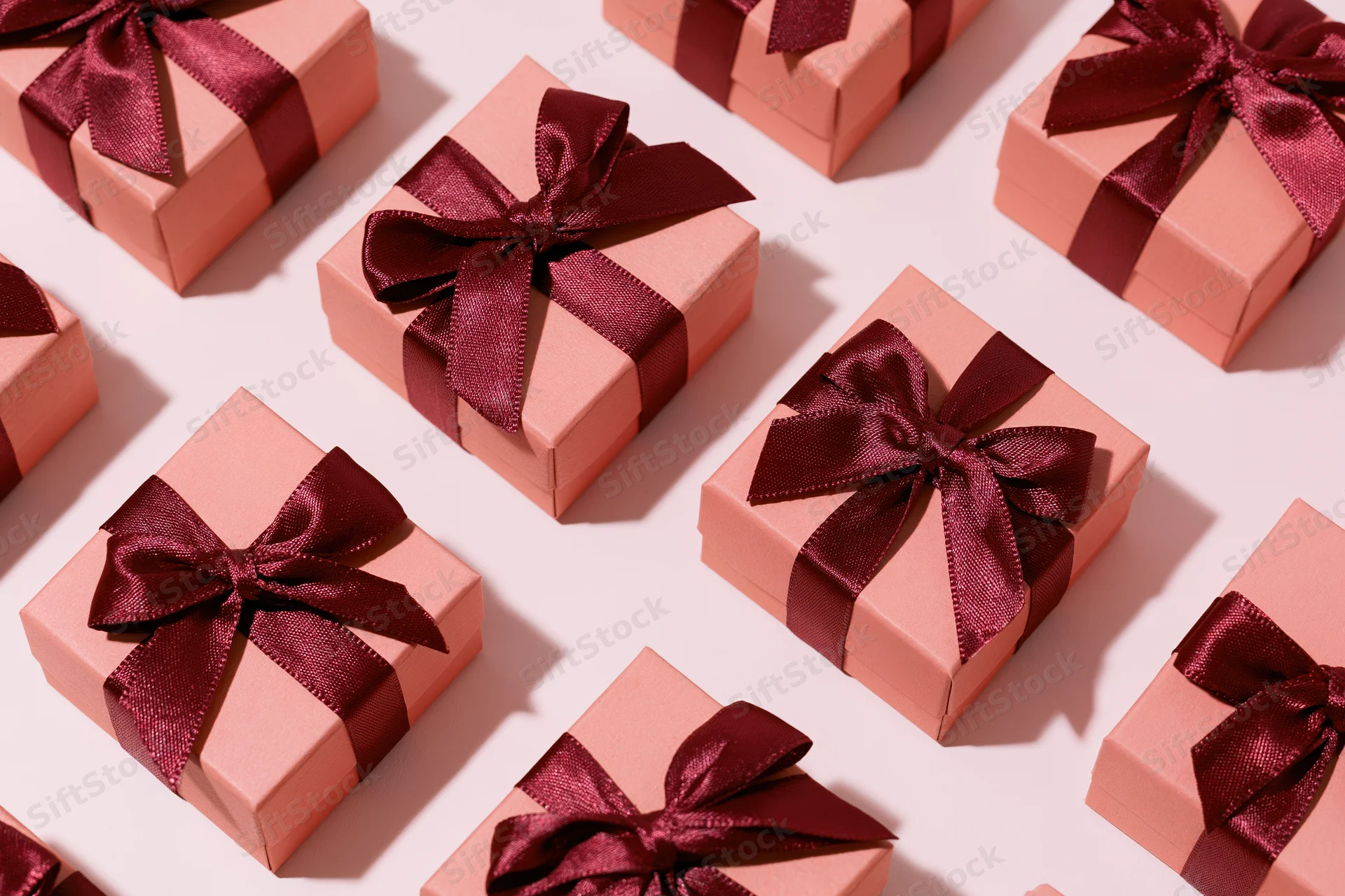 Multiple coral-pink gift boxes with burgundy satin bows arranged in flat lay overhead view on white background