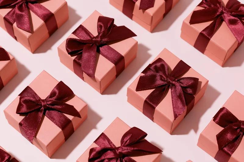 Multiple coral-pink gift boxes with burgundy satin bows arranged in flat lay overhead view on white background