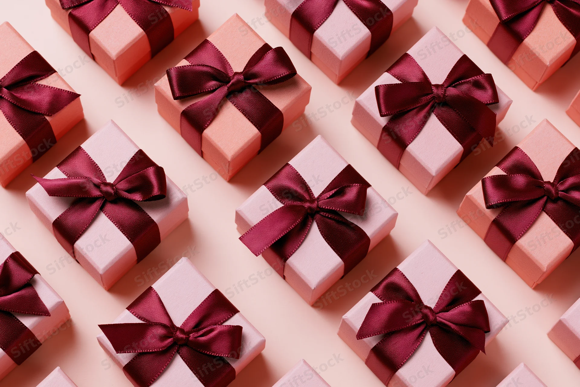 Coral-pink gift boxes with burgundy satin bows arranged in a flat lay pattern on a light pink surface