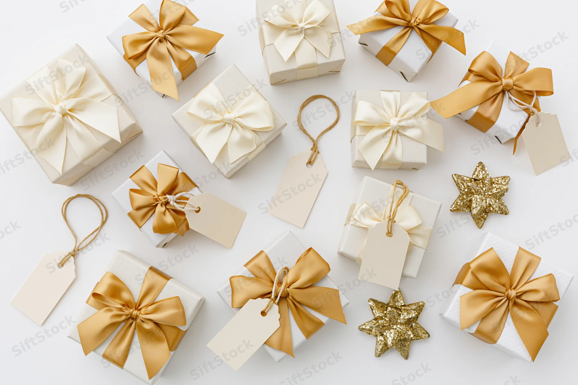 White gift boxes with gold and cream ribbons and tags arranged in flat lay on white background