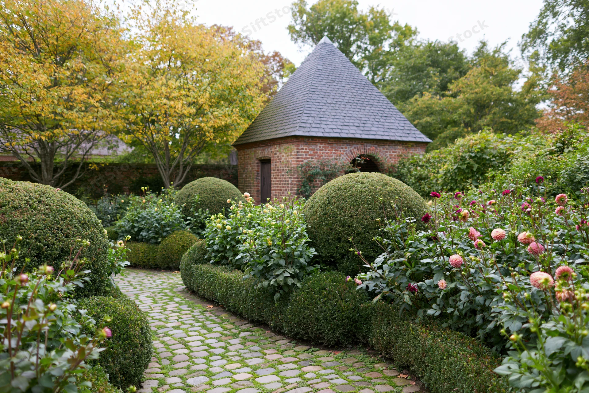 Formal european garden with brick gazebo and topiary hedges along a cobblestone pathway in early autumn