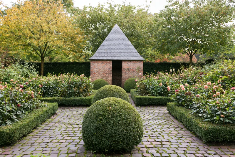 Formal european garden with brick gazebo and topiary along cobblestone pathway in early autumn