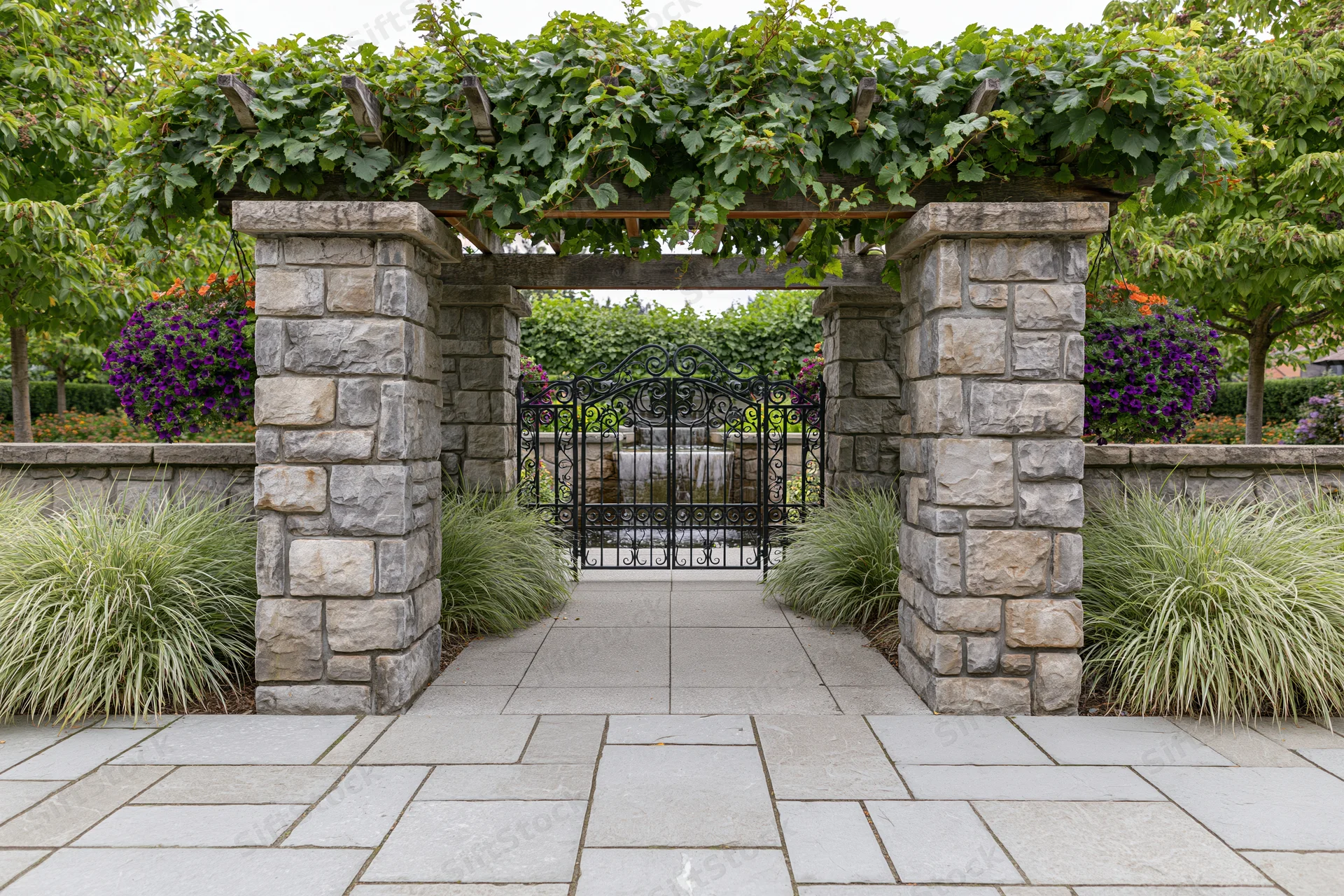 Stone pillar pergola framing a wrought iron gate in a formal garden courtyard
