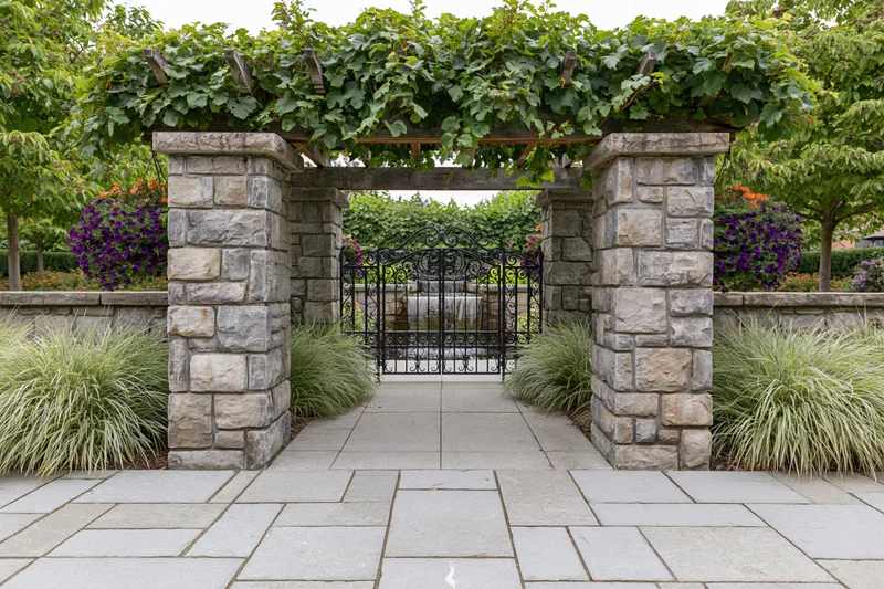 Stone pillar pergola framing a wrought iron gate in a formal garden courtyard