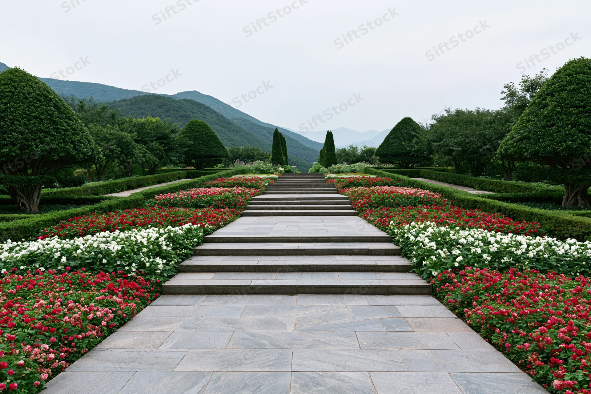 Stone steps leading through a symmetrical garden with red and white flowers and topiary hedges toward distant mountains