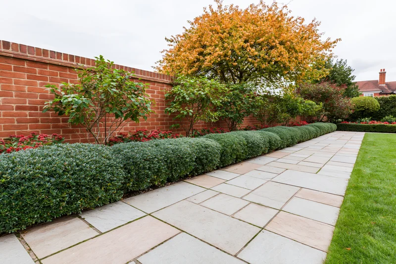 Formal garden with trimmed hedge along stone pathway beside red brick wall