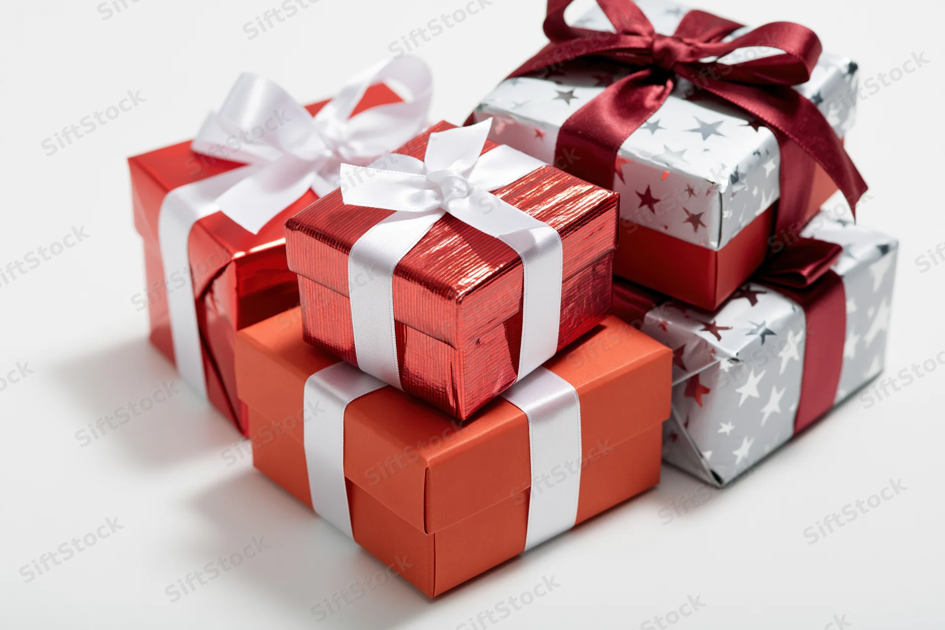 Stacked gift boxes wrapped in red and silver paper with ribbons on white surface