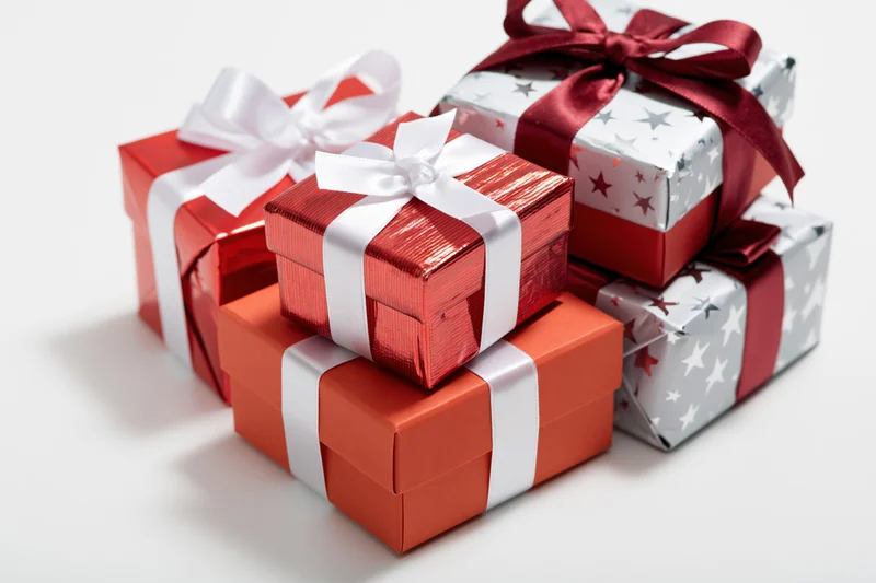 Stacked gift boxes wrapped in red and silver paper with ribbons on white surface