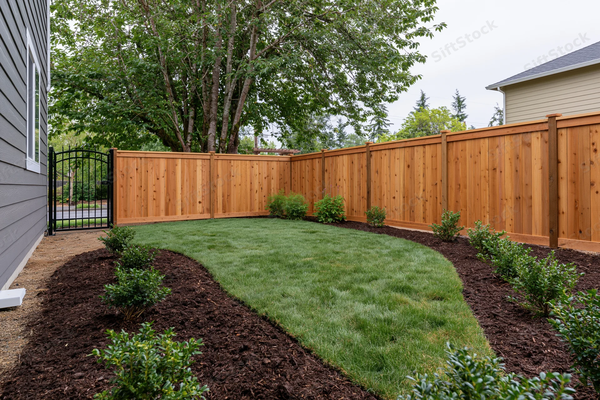 Freshly landscaped residential backyard with wooden fence and mulched garden beds surrounding a green lawn