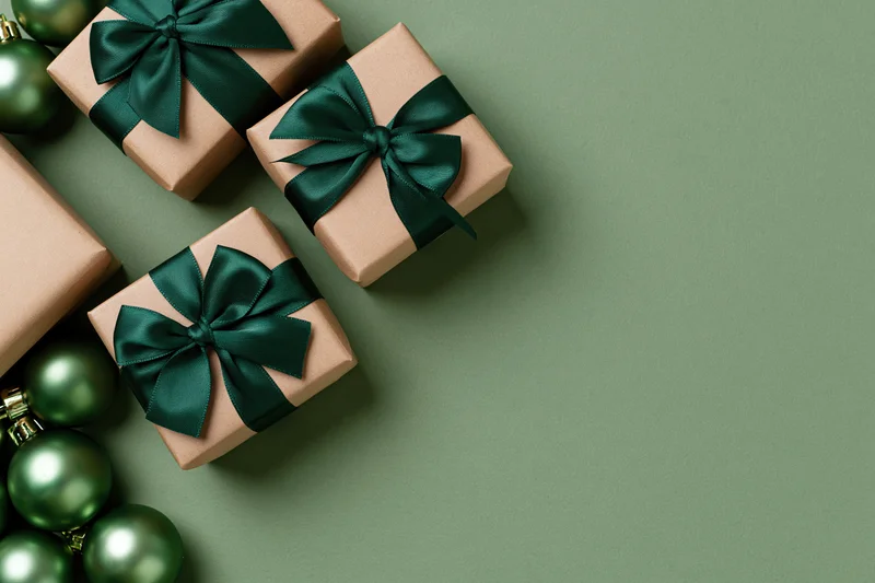 Gift boxes wrapped in kraft paper with dark green satin ribbons and ornaments on a green surface
