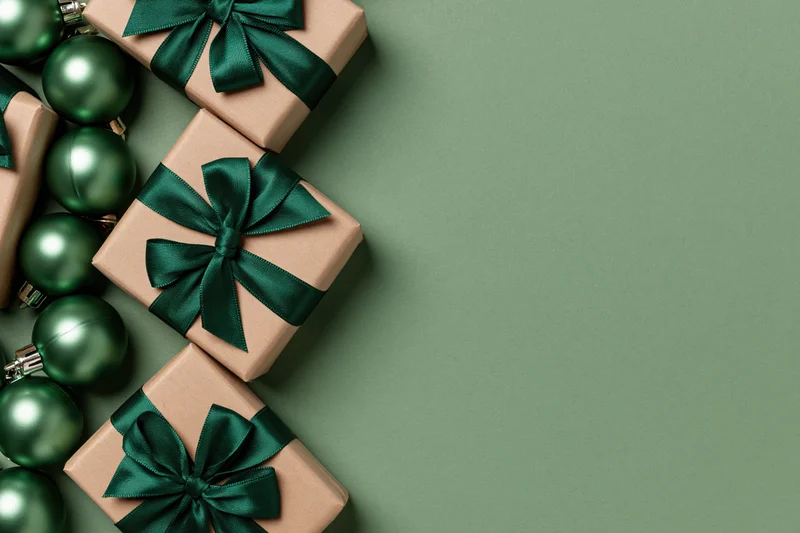 Gift boxes wrapped in kraft paper with dark green satin ribbons and ornaments arranged on a green surface