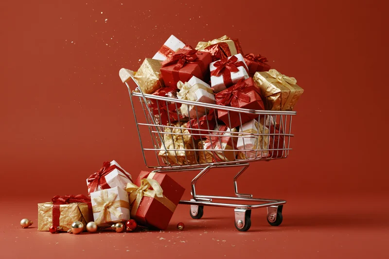 Metal shopping cart overflowing with wrapped christmas gifts on red background