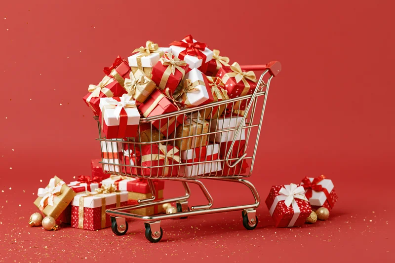 Metal shopping cart overflowing with wrapped christmas gifts on red background