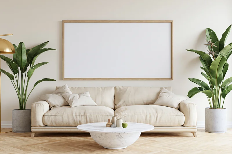 Minimalist scandinavian living room with beige sofa, marble coffee table, potted banana plants, and blank framed wall art