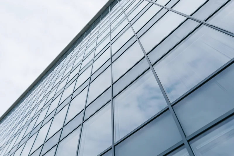 Low-angle view of modern glass office building facade reflecting sky and clouds