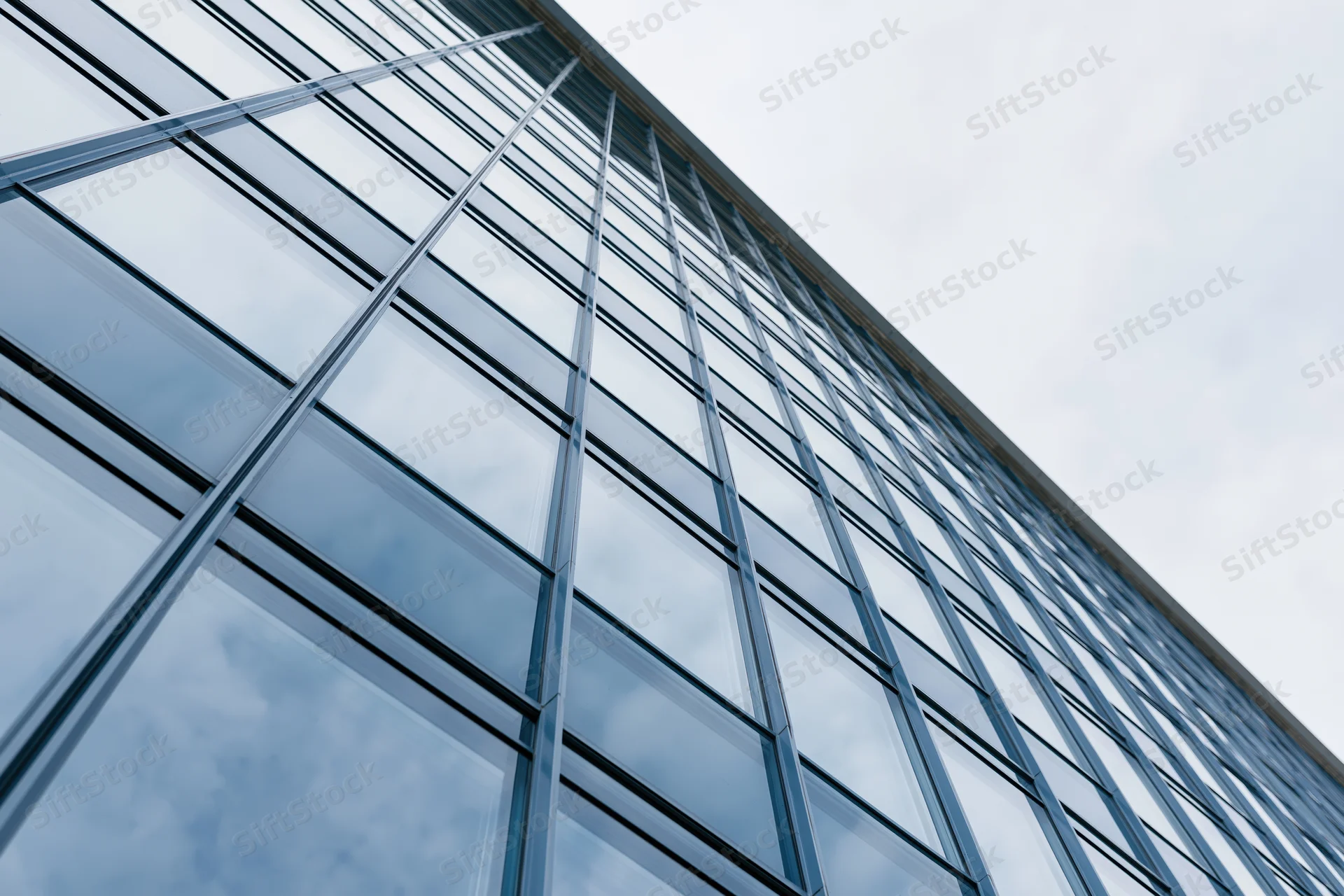 Low-angle view of modern glass office building facade reflecting sky and clouds
