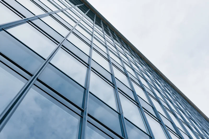 Low-angle view of modern glass office building facade reflecting sky and clouds