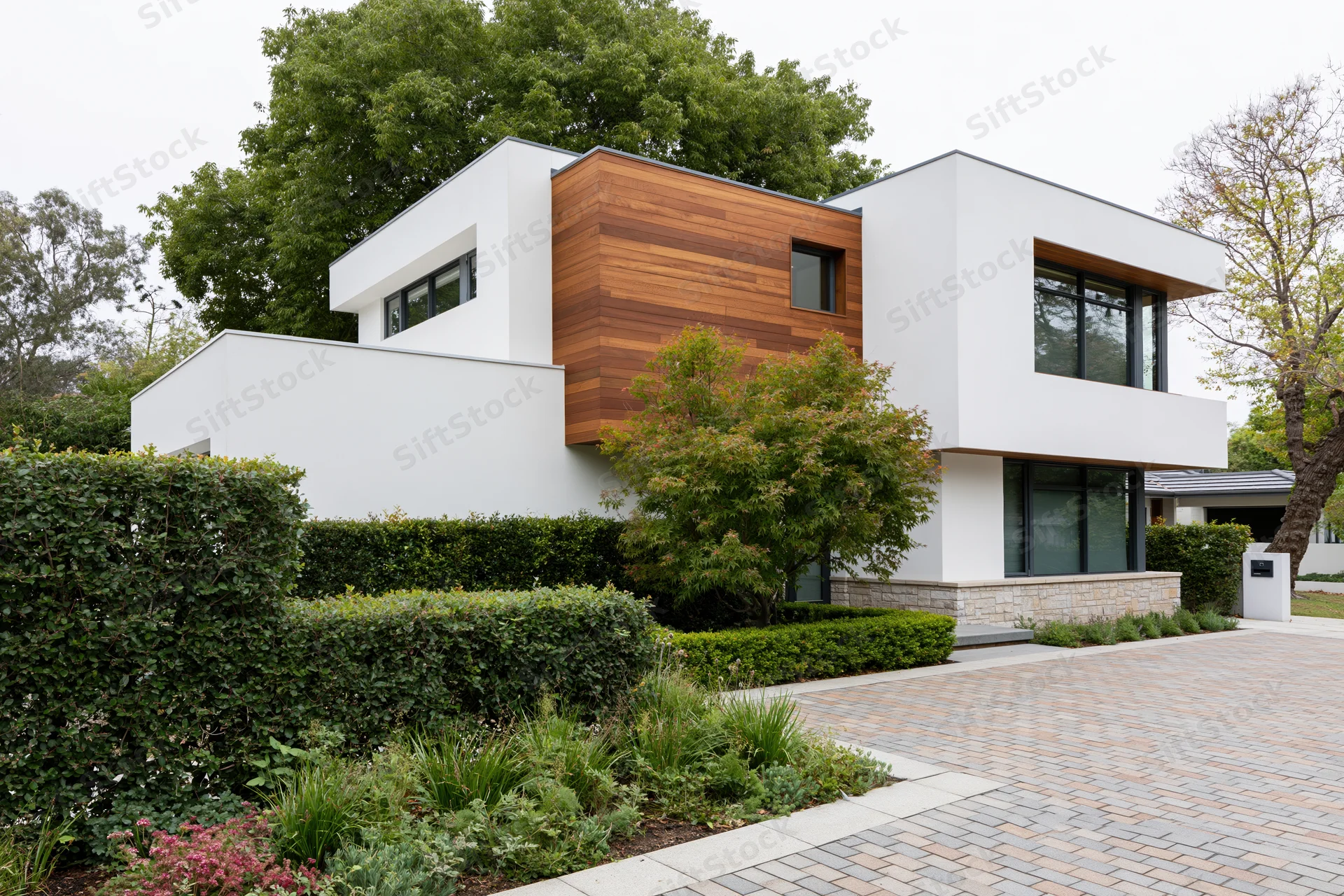 Modern two-story house with white and wood exterior surrounded by green landscaping and paved driveway