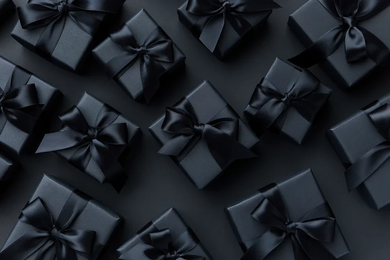 Multiple black gift boxes wrapped in matte black paper with satin ribbons arranged on dark surface
