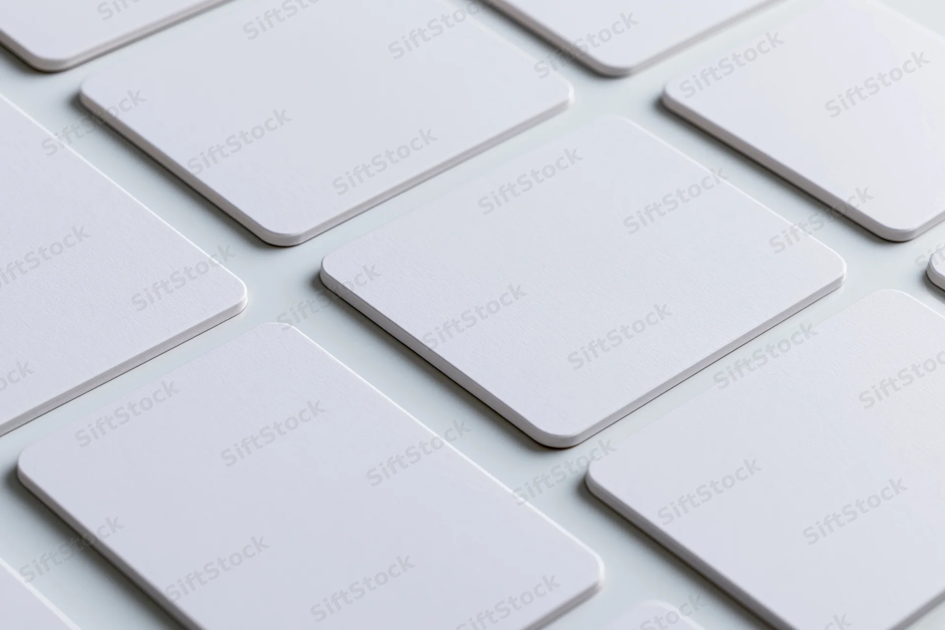 Blank white business cards with rounded corners arranged in a grid pattern on a light surface
