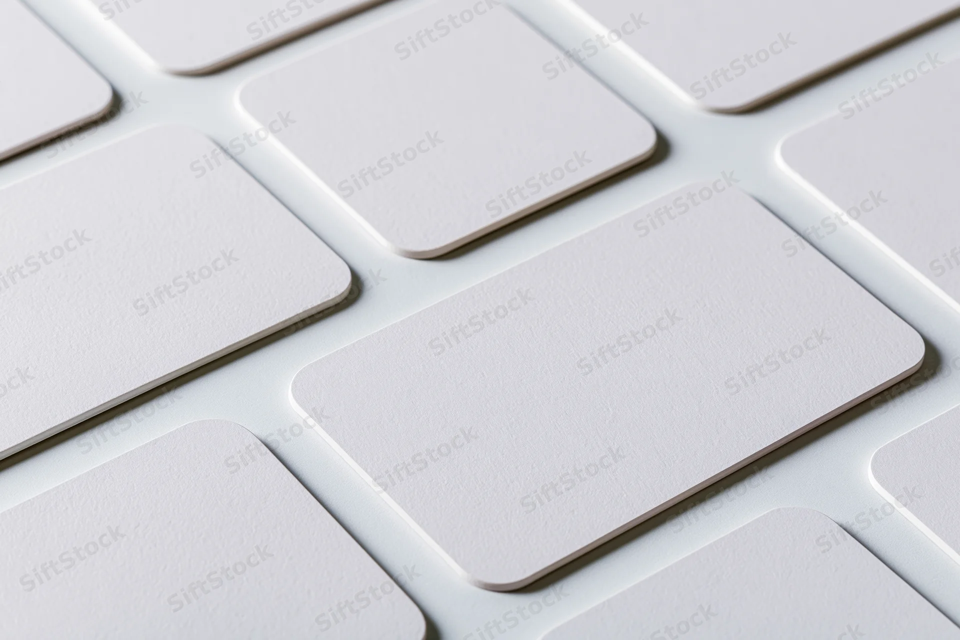 Blank white business cards with rounded corners arranged in a grid pattern on a flat surface