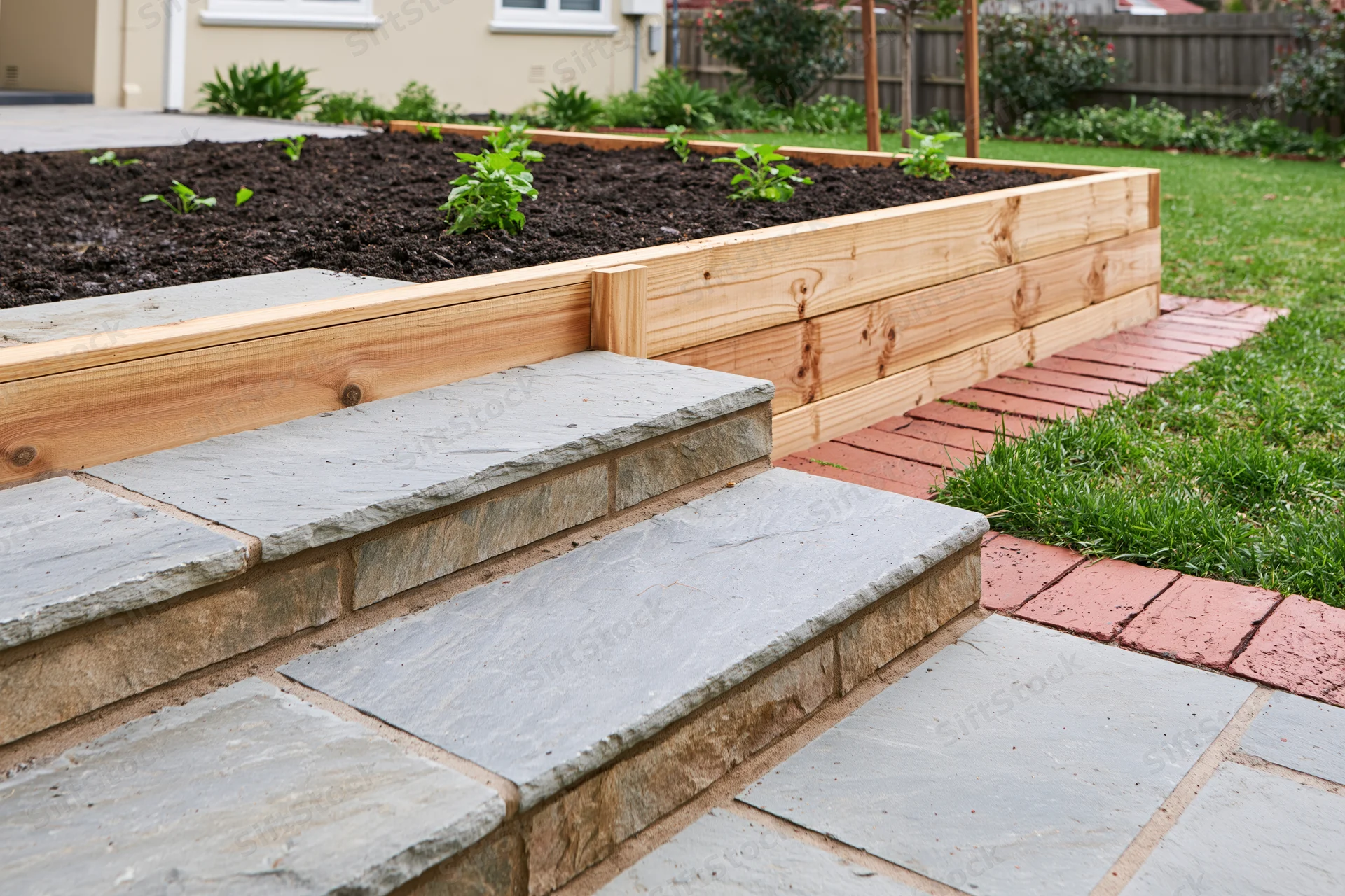 Raised garden bed made of pine wood with stone steps and brick pathway in a backyard garden