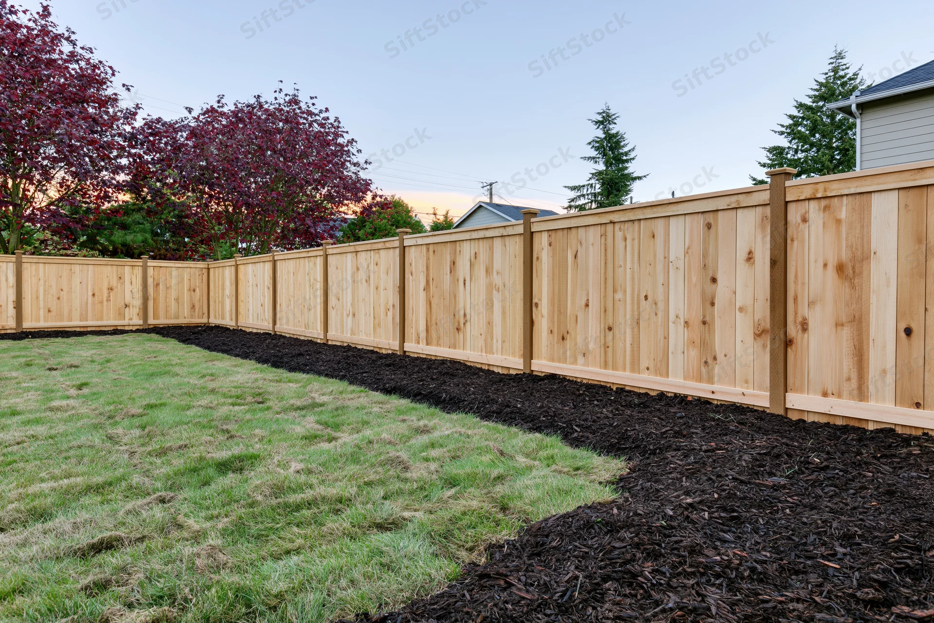 Wooden fence lining a newly landscaped suburban backyard with fresh sod lawn and mulched border