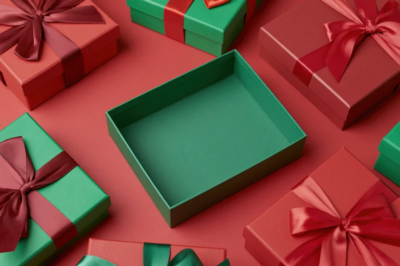 Open empty green gift box surrounded by closed red and green gift boxes with ribbons on a red surface