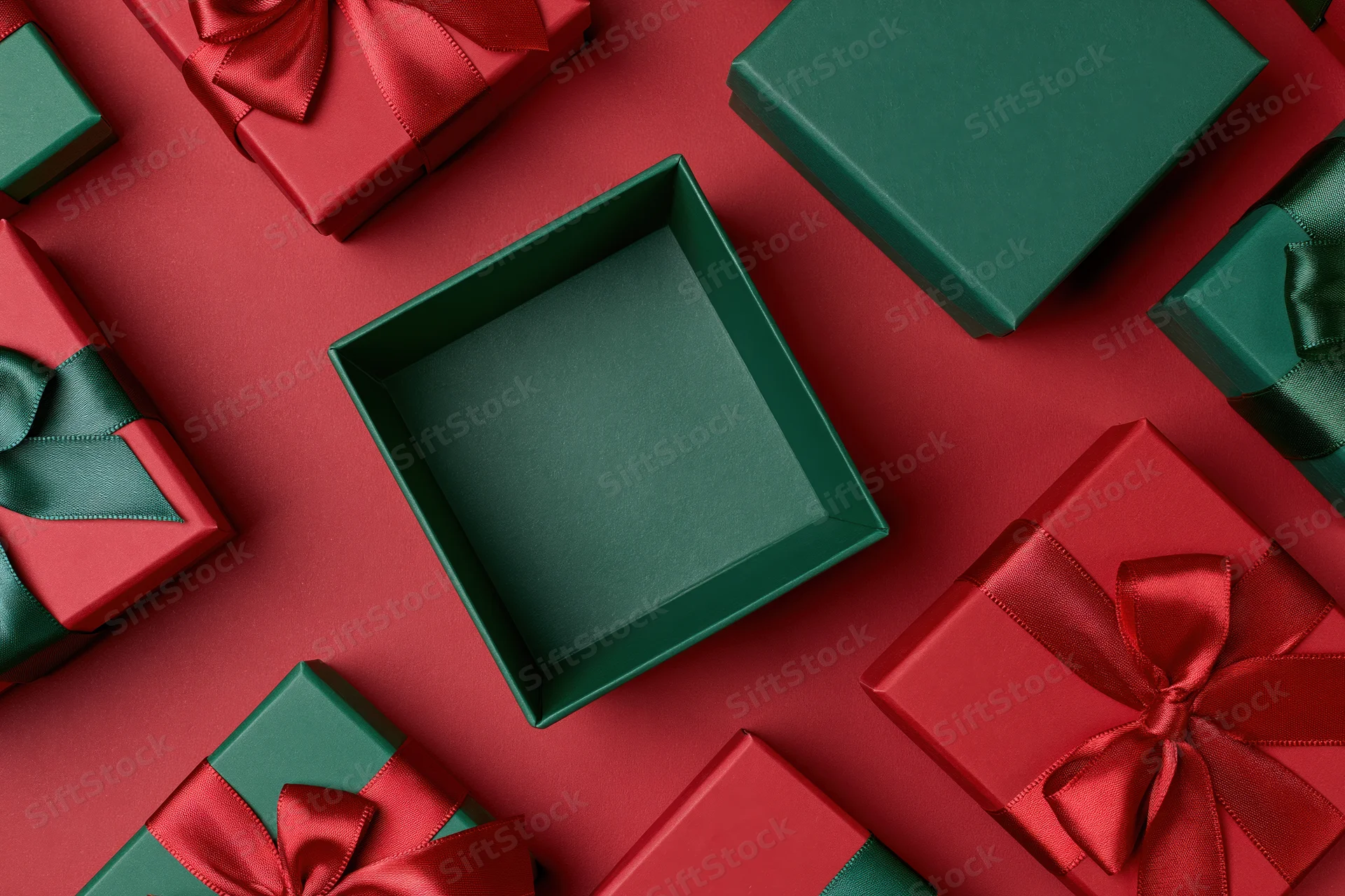 Open empty green gift box surrounded by closed red and green gift boxes on red surface
