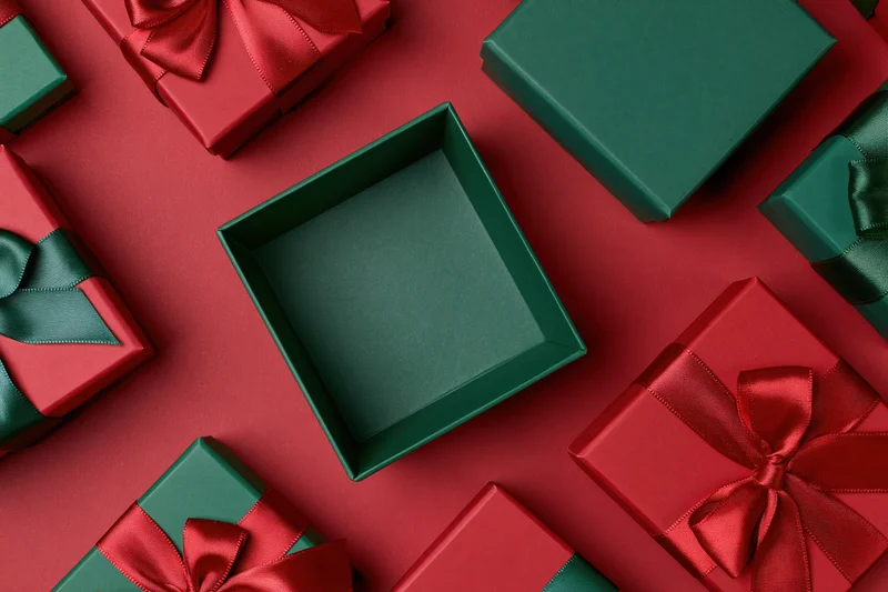 Open empty green gift box surrounded by closed red and green gift boxes on red surface