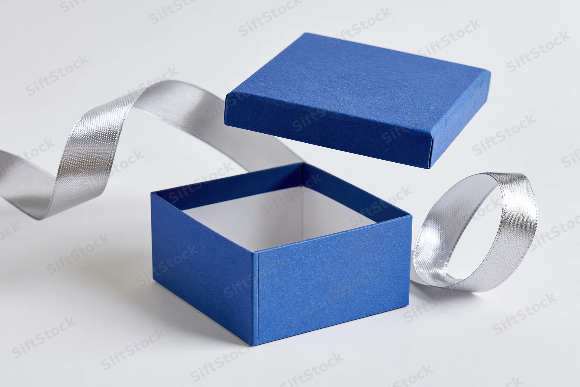 Open blue gift box with lid floating above and silver ribbon on white background