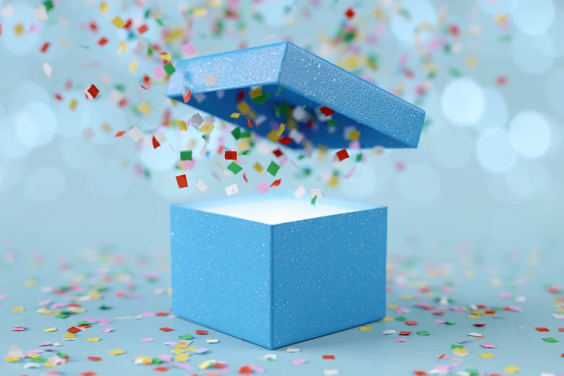 Open blue gift box with lid flying upward and multicolored confetti bursting out