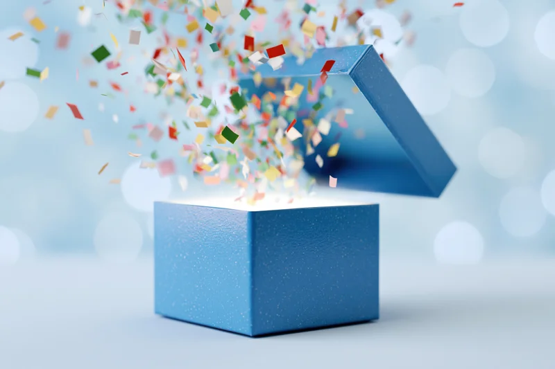 Open blue gift box with lid flying upward and multicolored paper confetti bursting out