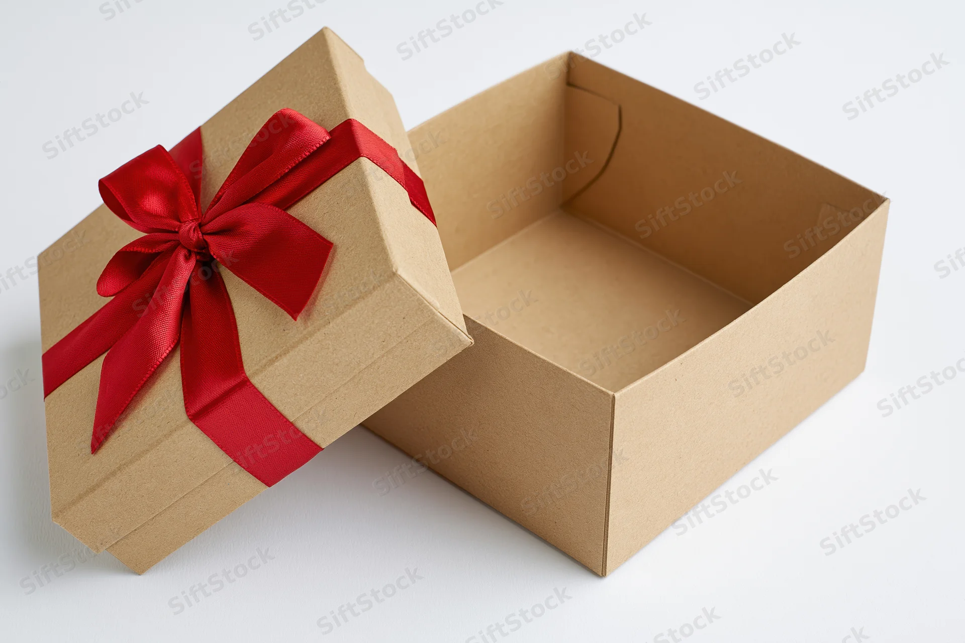 Open kraft cardboard gift box with red ribbon bow, lid propped aside on white background