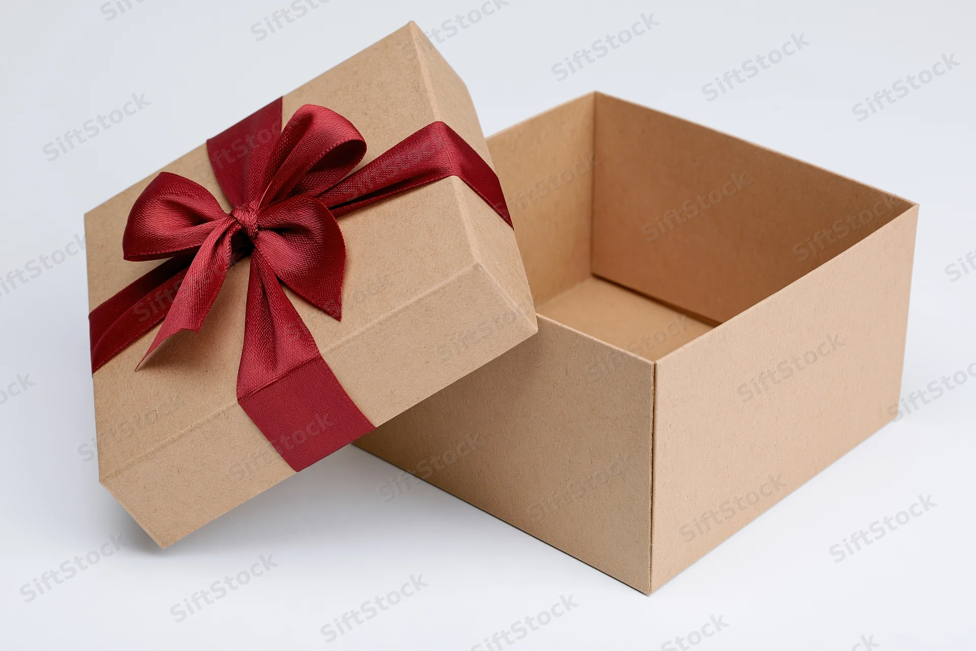 Open kraft cardboard gift box with red ribbon bow, lid propped aside on white background